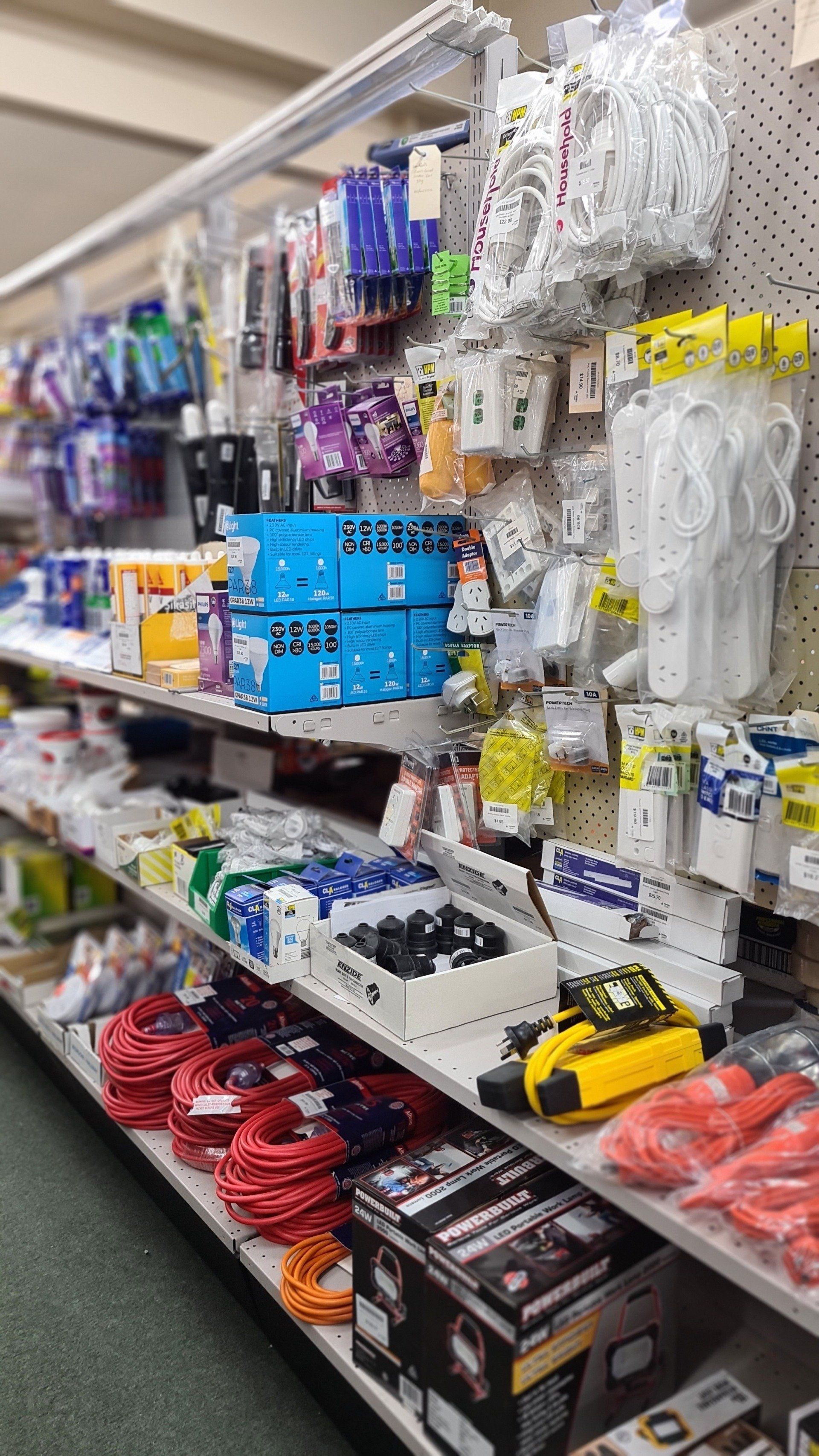 Retail shelving stocked with electrical cables, power strips, and various hardware supplies in a store aisle.