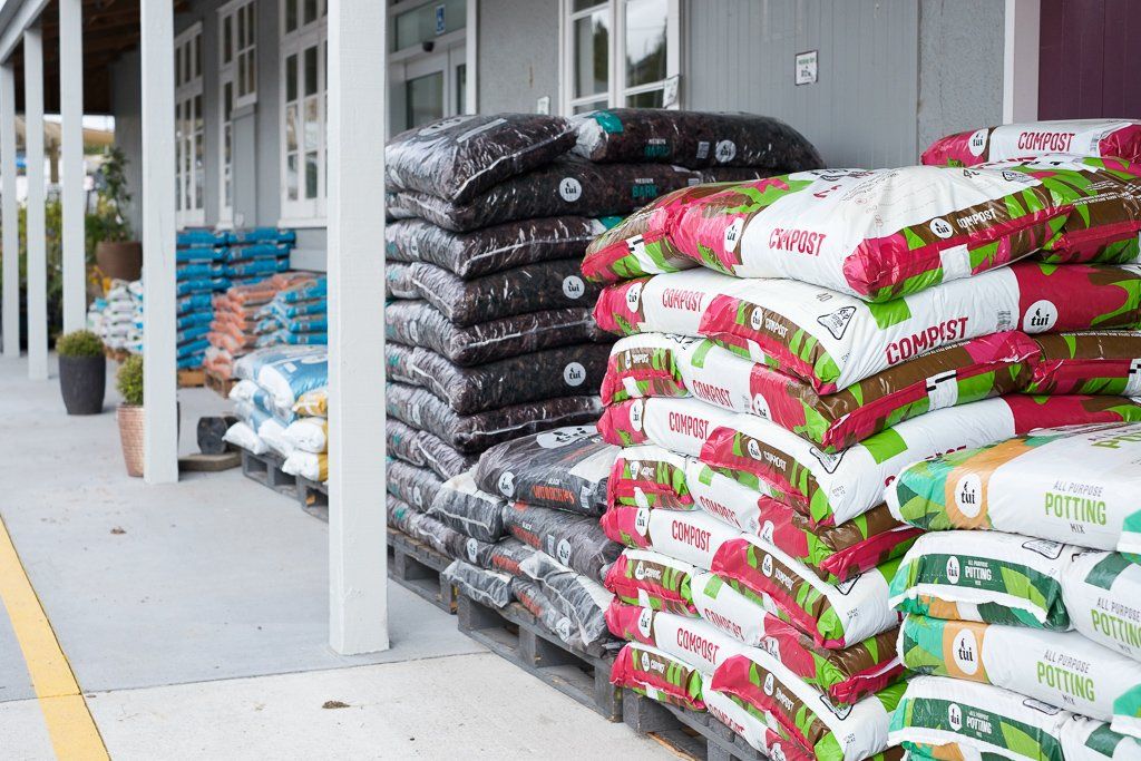 Stacks of bagged soil and mulch on pallets arranged along the exterior wall of a building.