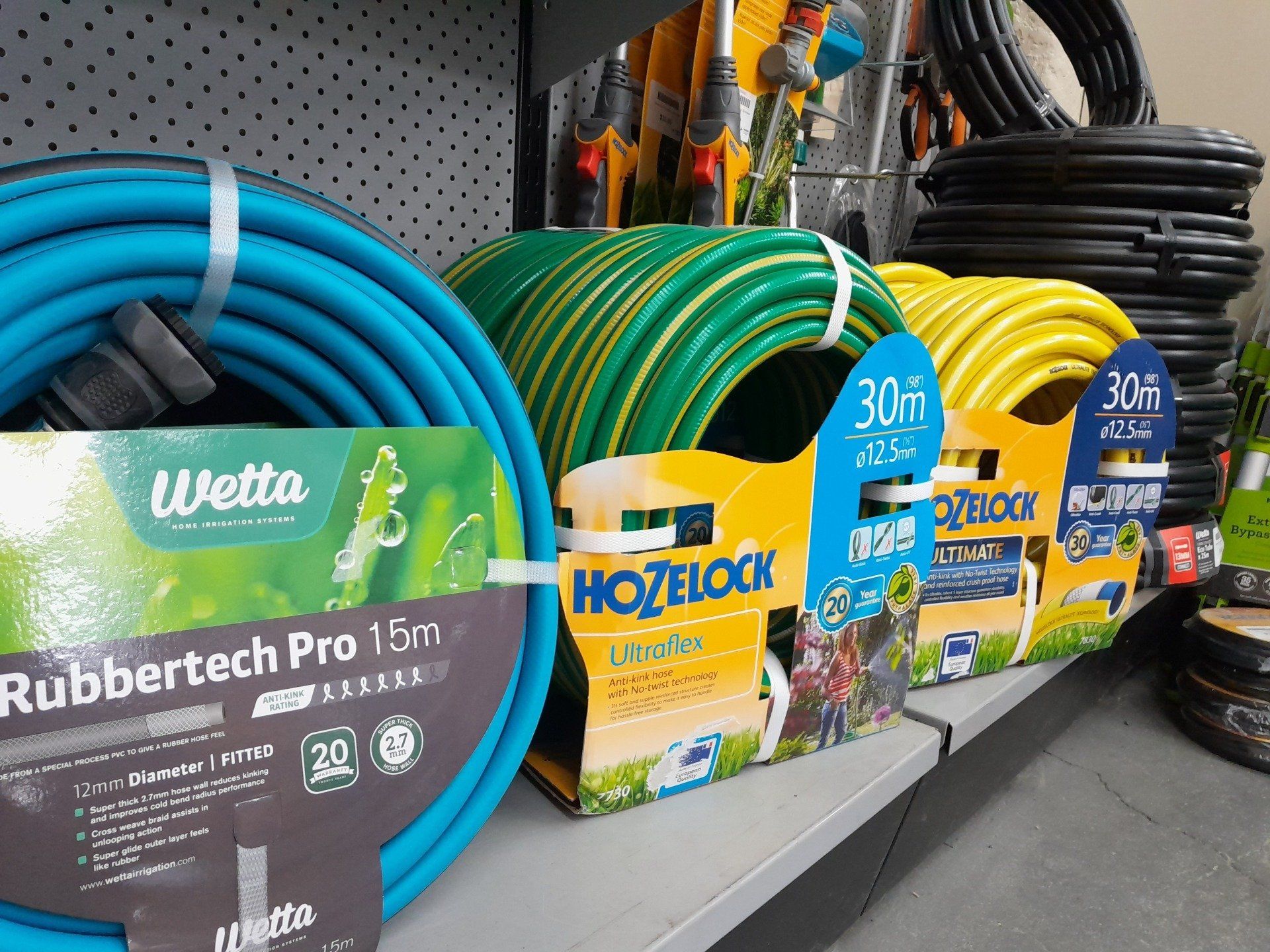 A display shelf in a store featuring multiple coiled garden hoses in shades of blue, green, and yellow.