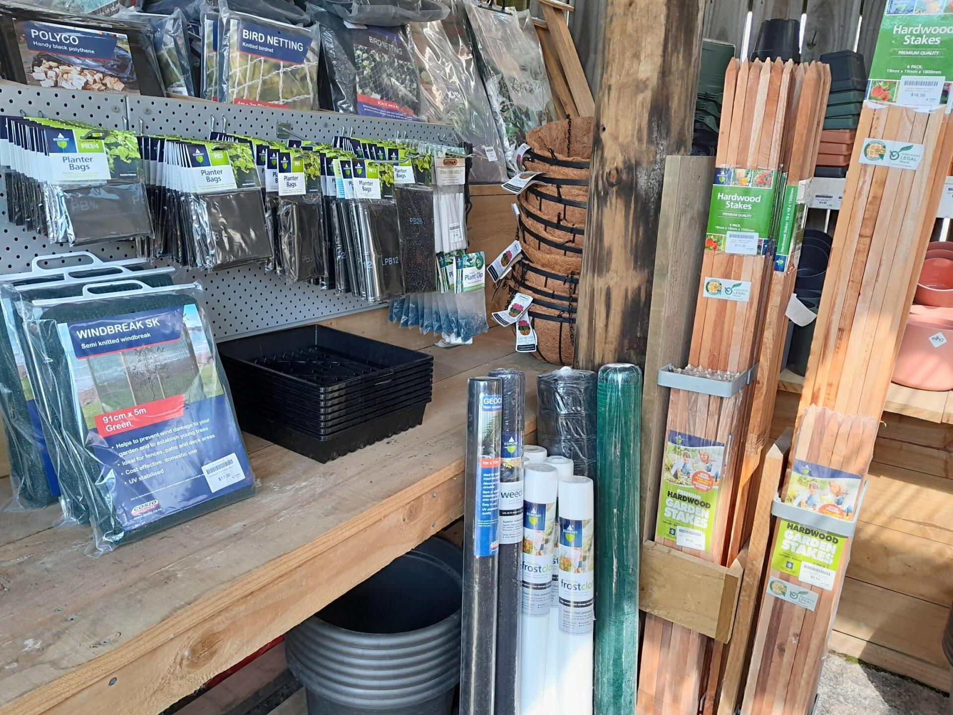 Shelves in a garden center filled with plant pots, wooden stakes, netting, and various gardening supplies.