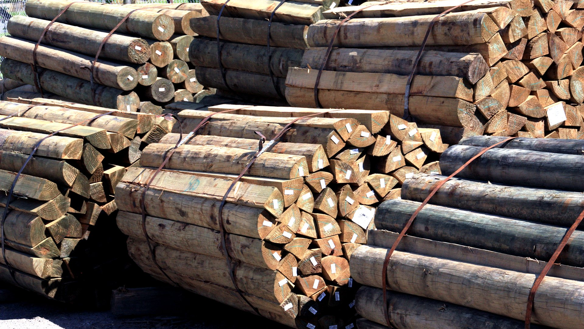 Bundles of brown wooden logs and timber poles stacked together in an outdoor yard.