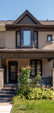 Townhouse exterior with light brown brick, black trim windows, and a covered porch with greenery.