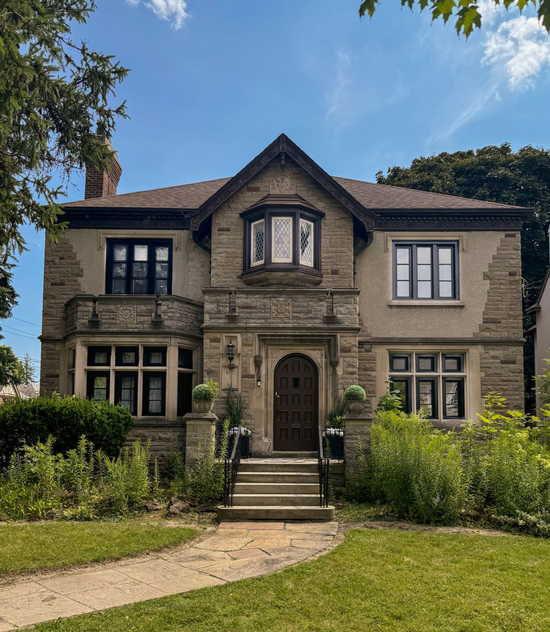 Two-story brick house with white trim. Bay windows, white front door, and a small front yard.