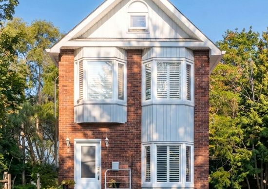 Two-story brick house with white trim. Bay windows, white front door, and a small front yard.