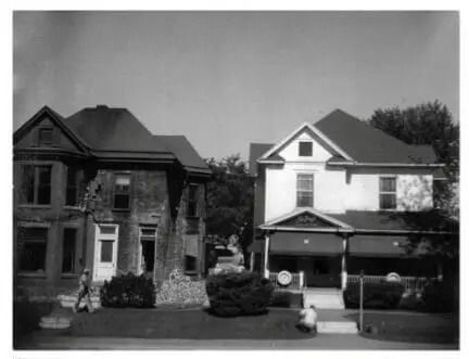 Two suburban houses side by side, one dark brick and one white with a porch, in black and white.