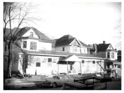 Black-and-white street view of a row of old houses with parked cars in front