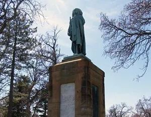 Statue atop a brick pedestal in a park with bare trees in winter