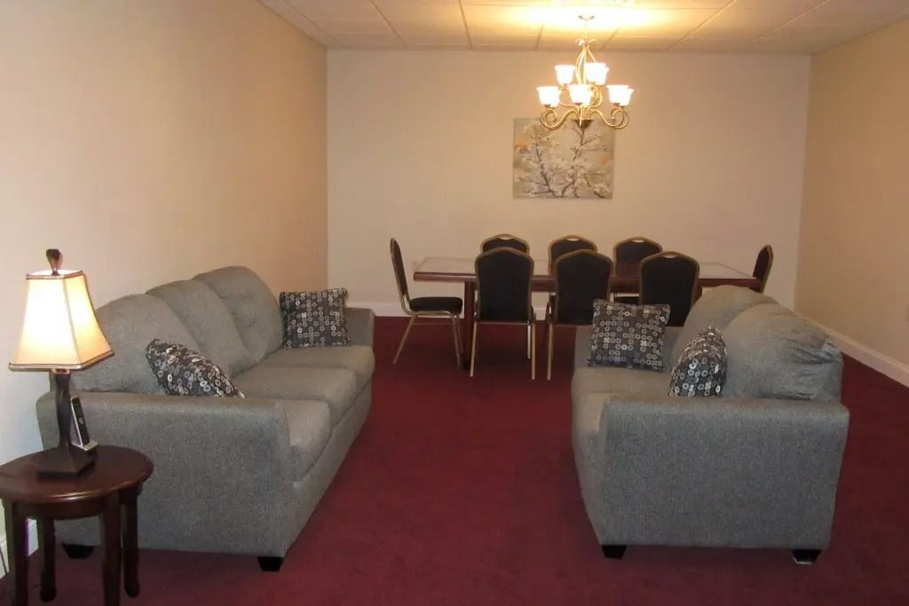 Small living room with two gray sofas, red carpet, and dining table under a chandelier