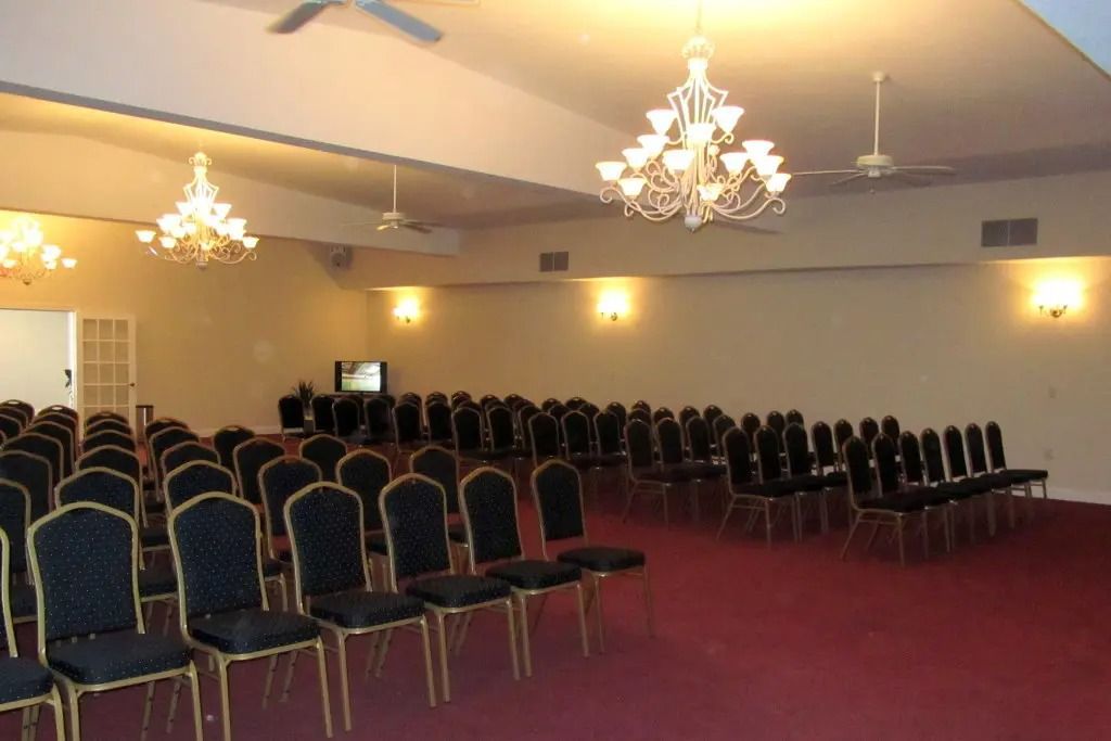 Empty banquet hall with rows of chairs, chandeliers, and maroon carpet lighting the room
