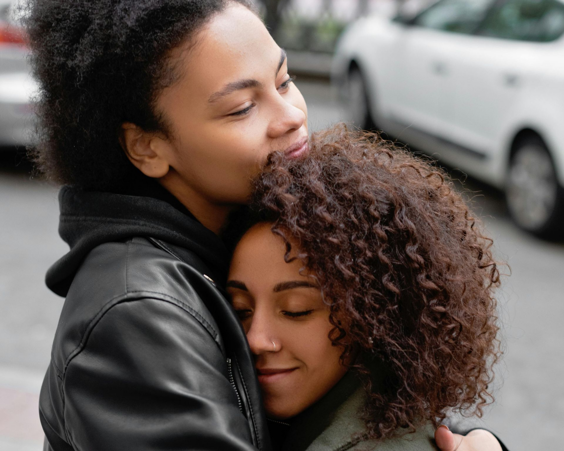 Two people embracing and smiling on a city street, with a white car blurred in the background
