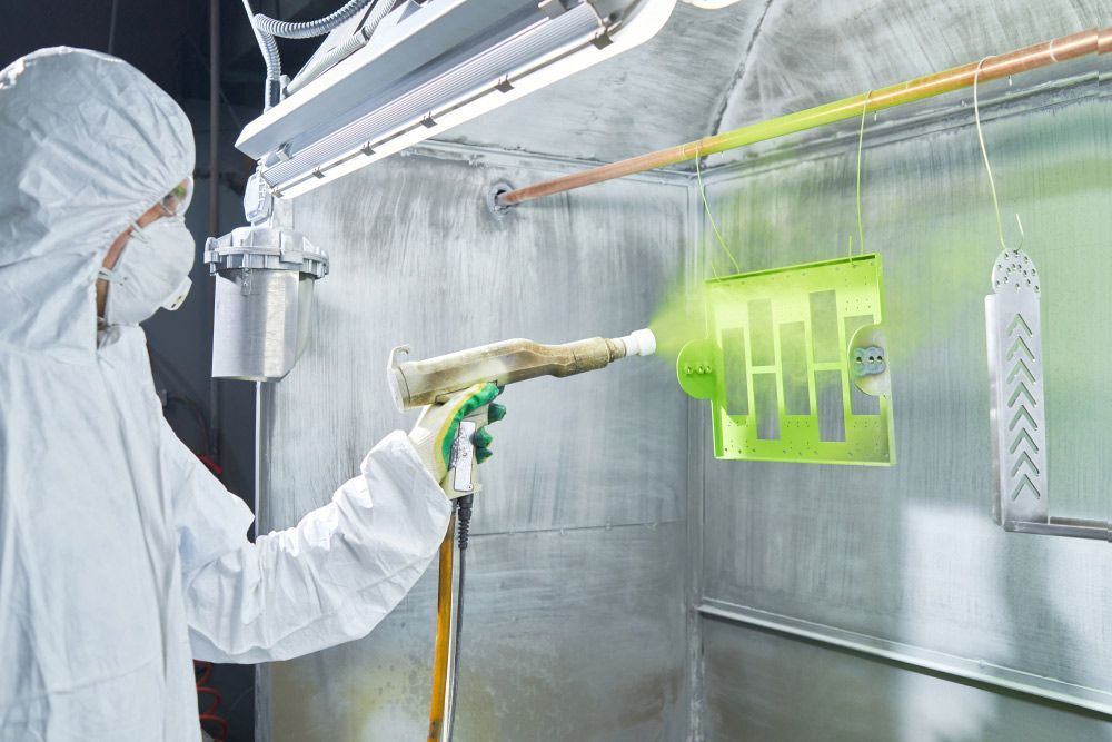 A Man in a Protective Suit is Spray Coating a Piece of Metal — Hastings Valley Powdercoaters in Harrington, NSW