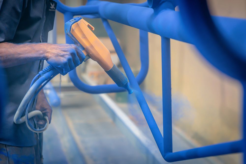 A Person is Spraying Blue Powder on a Metal — Hastings Valley Powdercoaters in South West Rocks, NSW