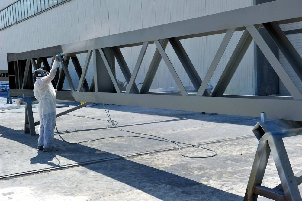 A Man in a White Suit is Spraying Powder on a Metal Structure — Hastings Valley Powdercoaters in Taree, NSW