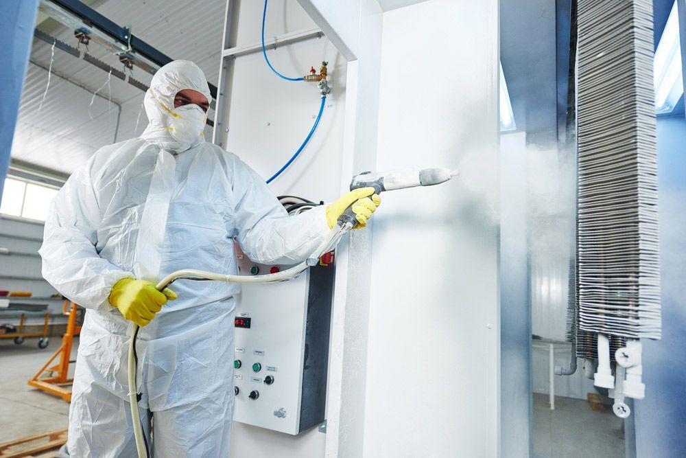 A Man in a Protective Suit is Spraying Powder — Hastings Valley Powdercoaters in Harrington, NSW