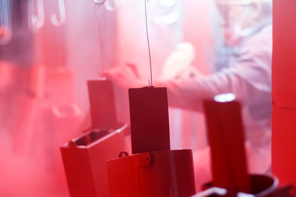 A Person is Coating a Piece of Metal With Red Paint — Hastings Valley Powdercoaters in Port Macquarie, NSW