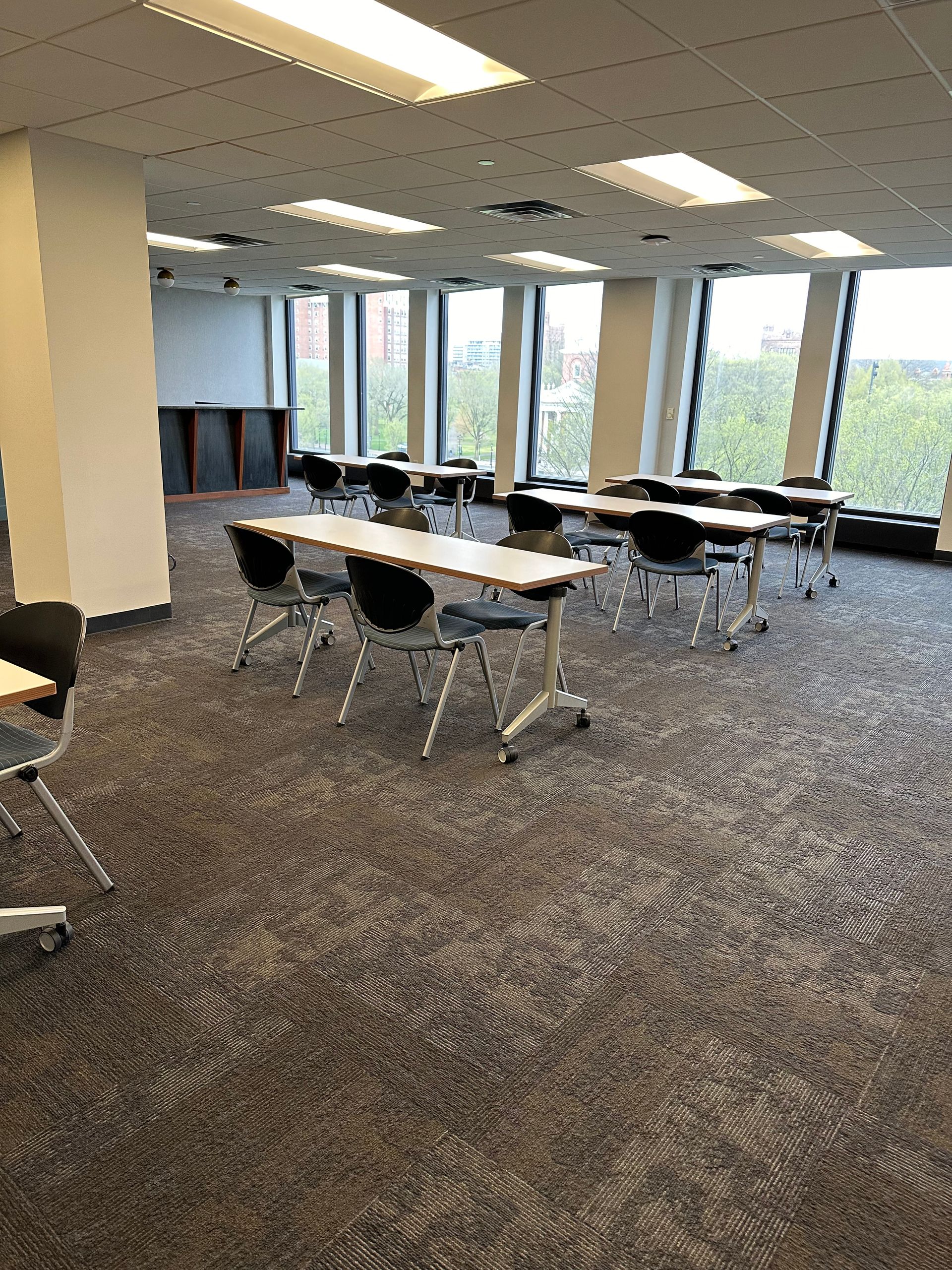 Empty conference room with tables and chairs, large windows, and patterned carpet.