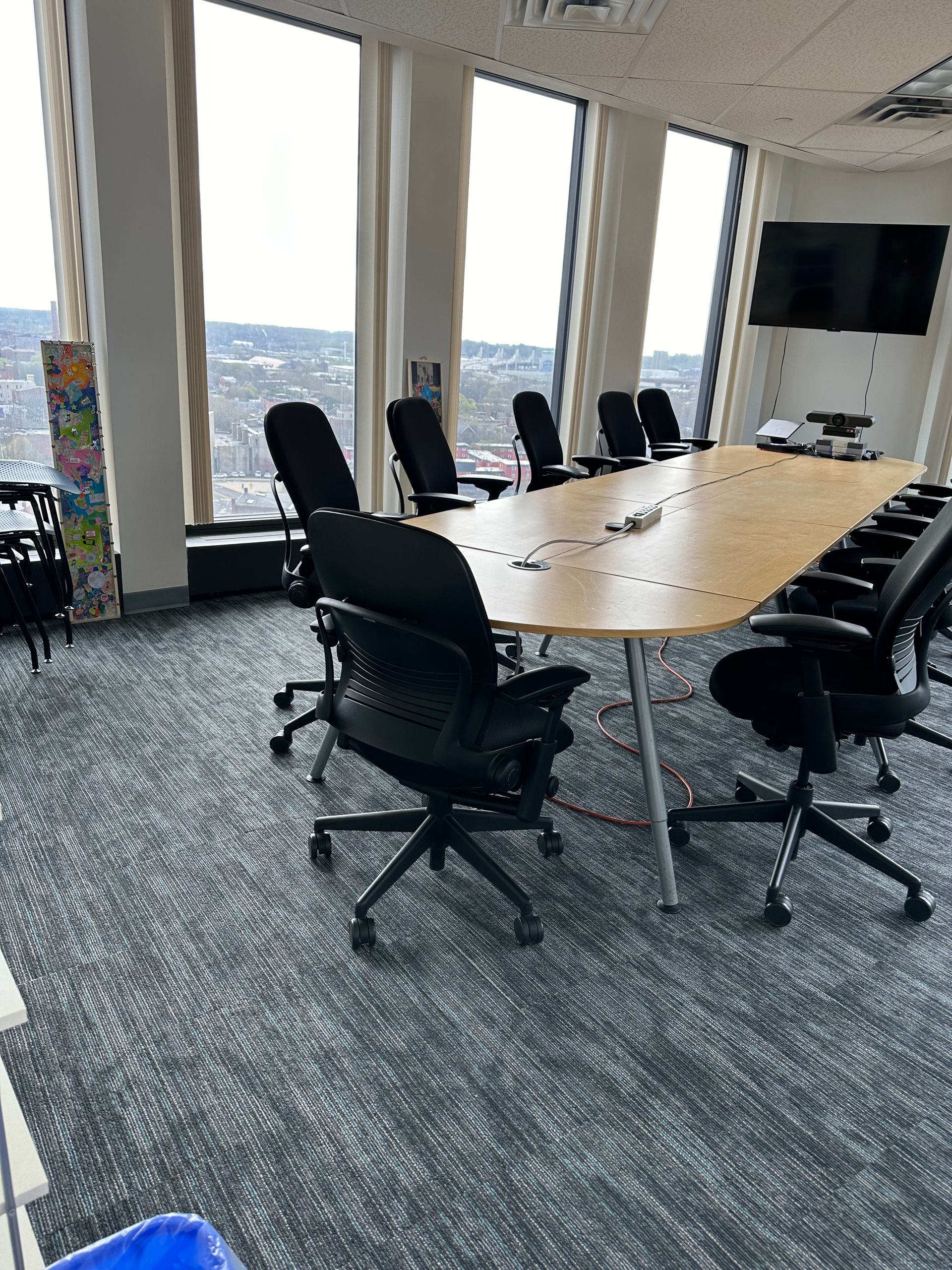 Modern conference room with a long wood table, black chairs, and large windows overlooking a city skyline.