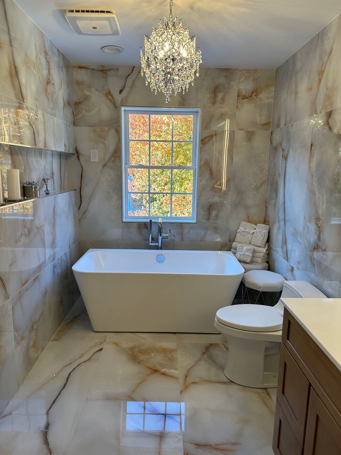 Marble bathroom with freestanding tub, toilet, chandelier, and window with autumn view