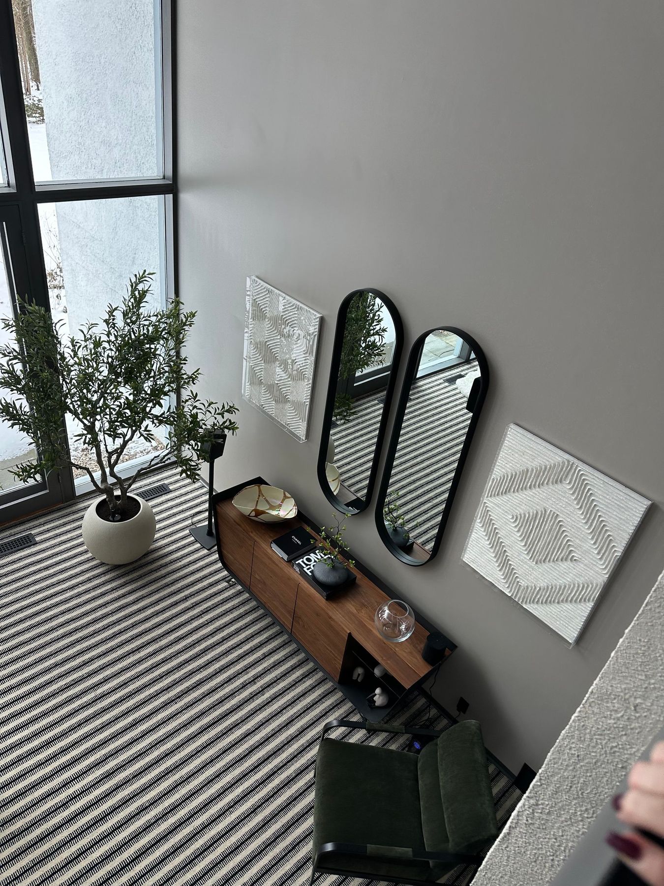Cozy room corner with a potted plant, wall mirrors, wood shelf, and patterned rug by a window
