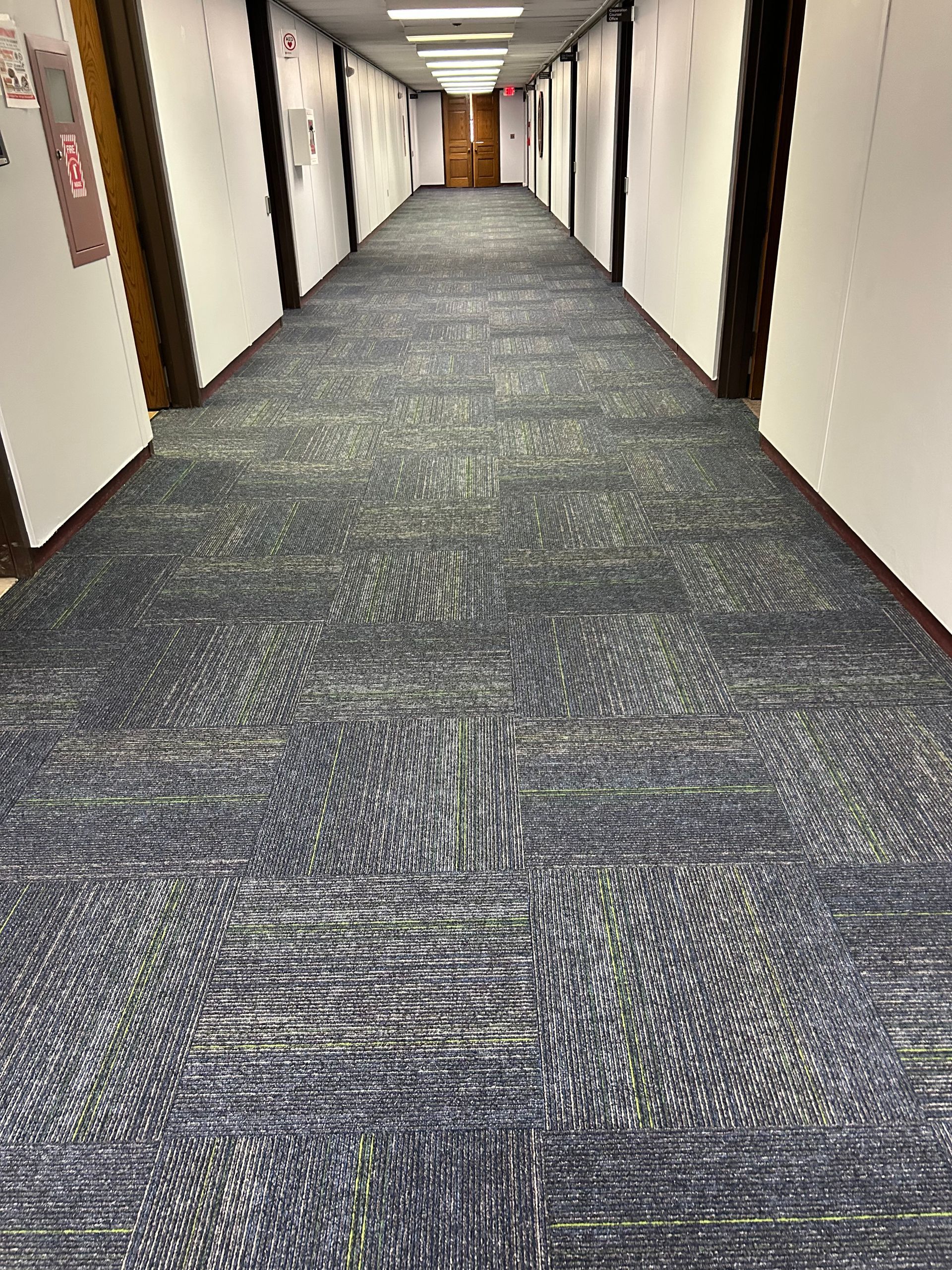 Long, empty office hallway with patterned gray carpet and white walls under fluorescent lights