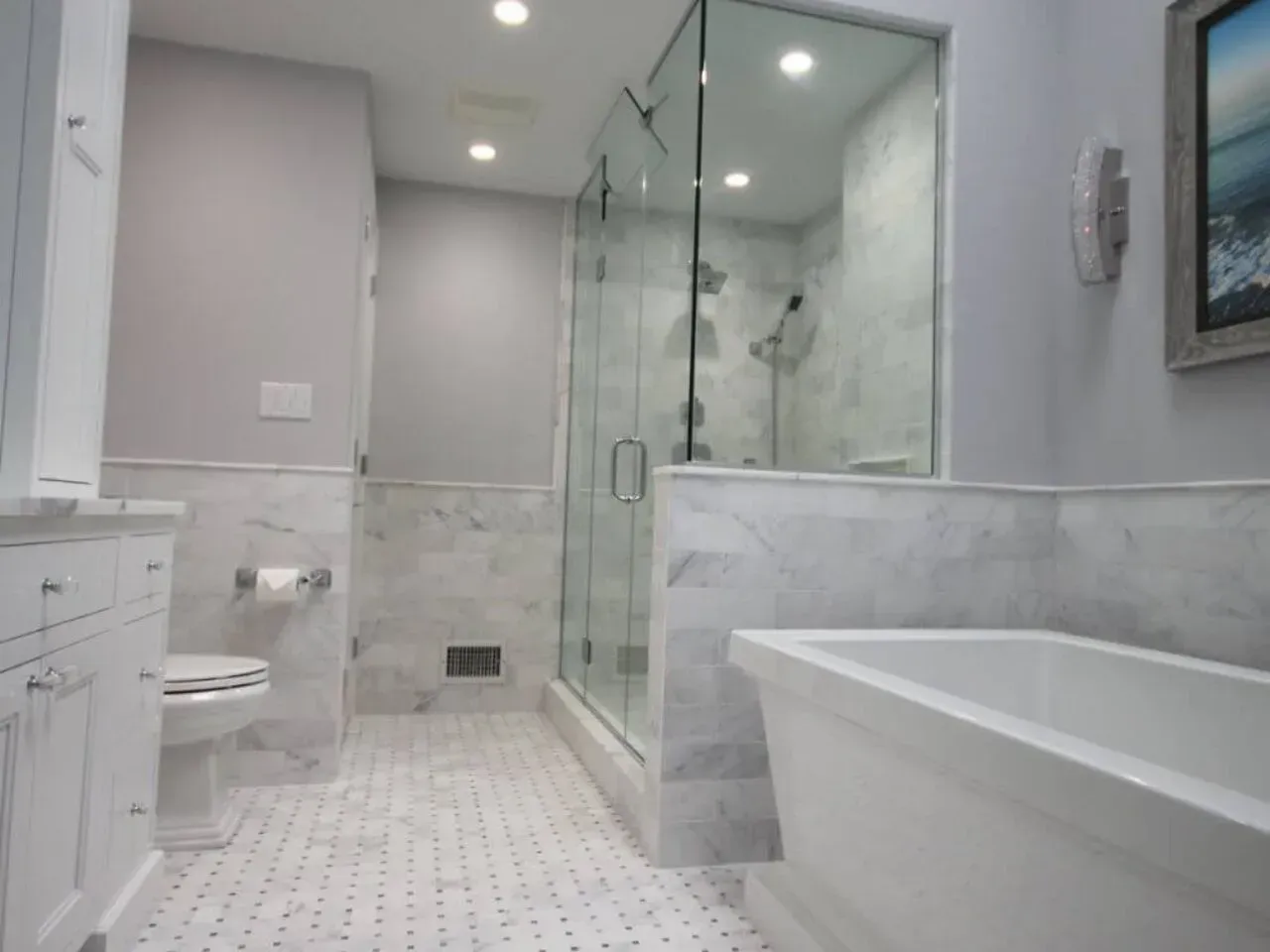 Modern white bathroom with marble tile, glass shower, and freestanding tub.