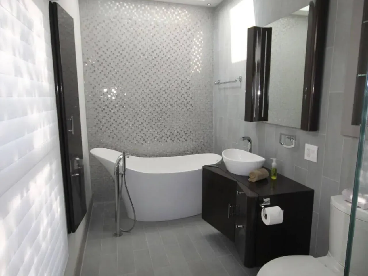 Modern bathroom with freestanding tub, dark wood cabinets, and gray tile.