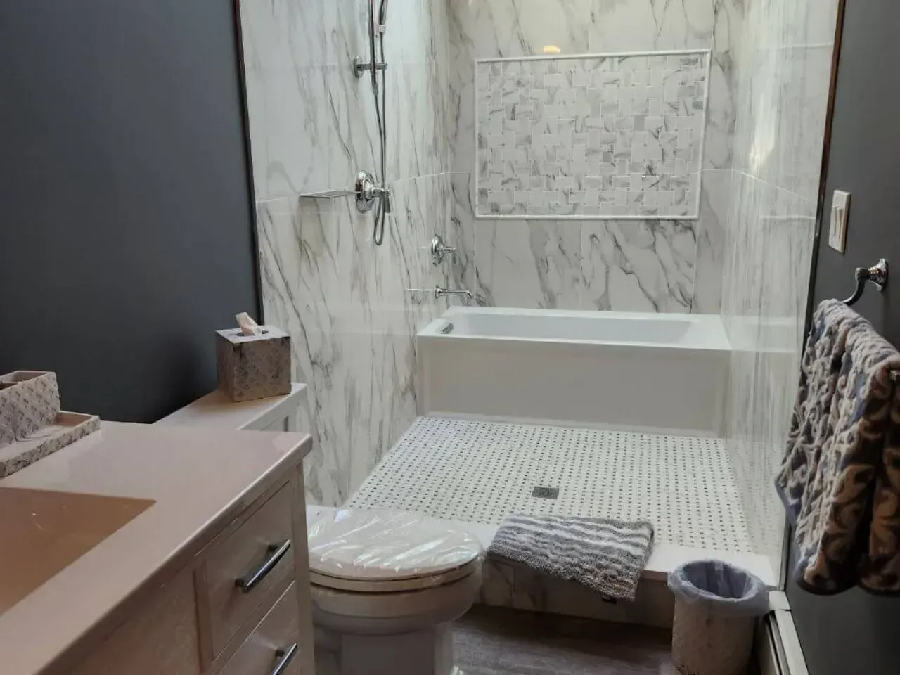 Bathroom with marble-look tile, white bathtub, toilet, and vanity, gray walls.