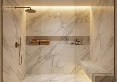 Luxurious marble shower with recessed shelf, bench, and gold fixtures.