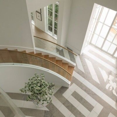 Bright atrium with curved staircase, large windows, and sunlight casting geometric shadows on the floor.