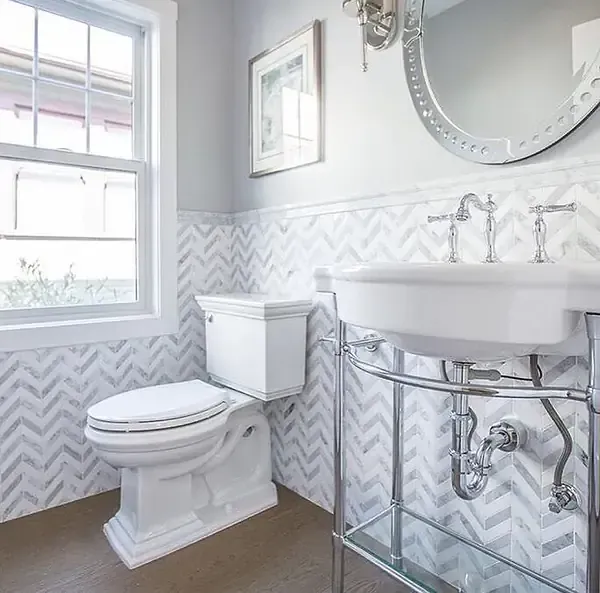 Elegant bathroom with white toilet, sink, and chevron-patterned tiled walls.