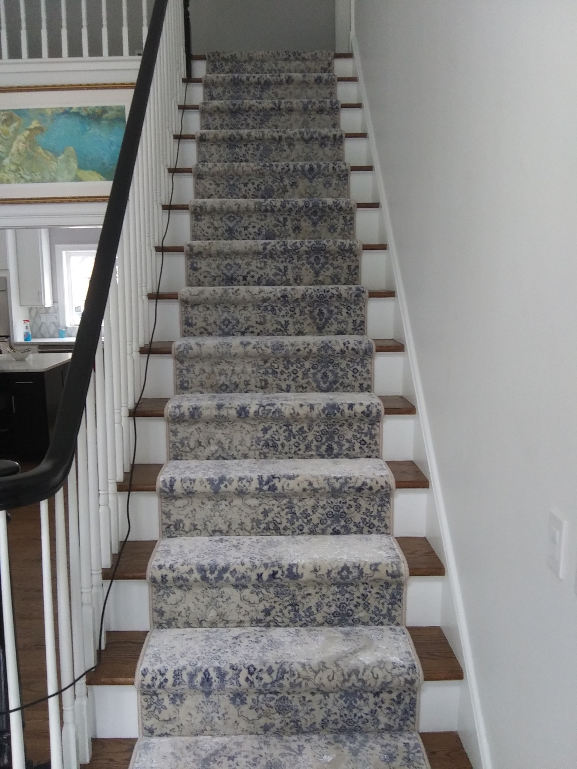 Carpeted staircase with patterned runner in a white interior hallway