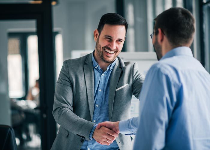 Two professionals shake hands in a modern office, smiling during a business meeting.