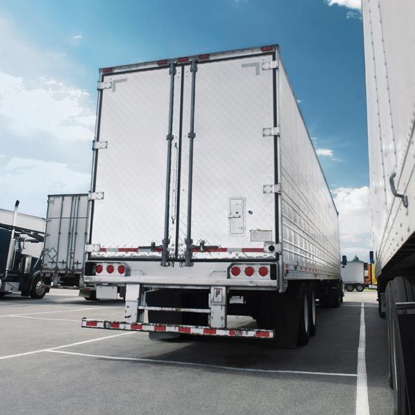 White semi-trailer truck parked in a lot beside another truck under a blue sky