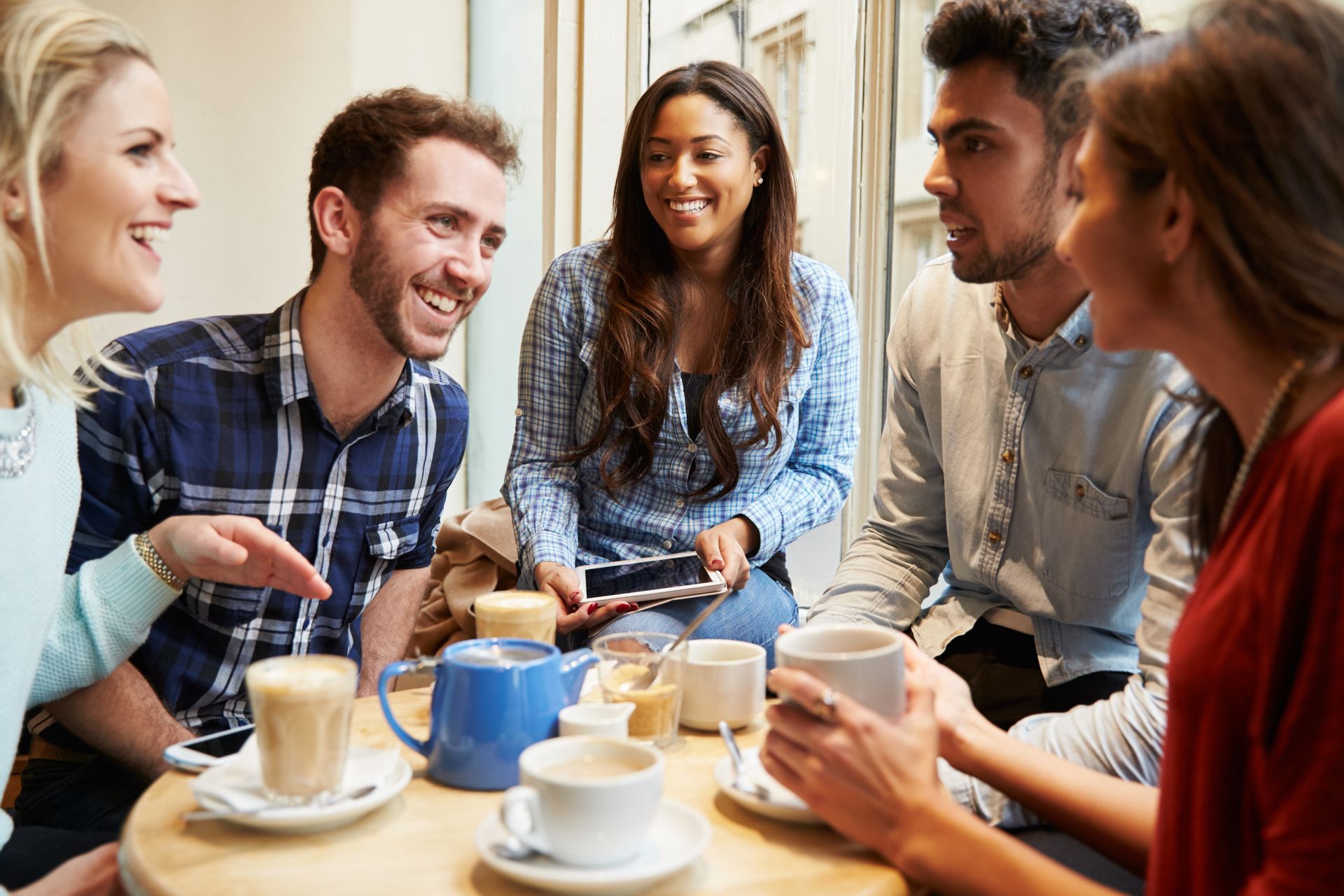 a group of people are sitting around a table drinking coffee and talking.