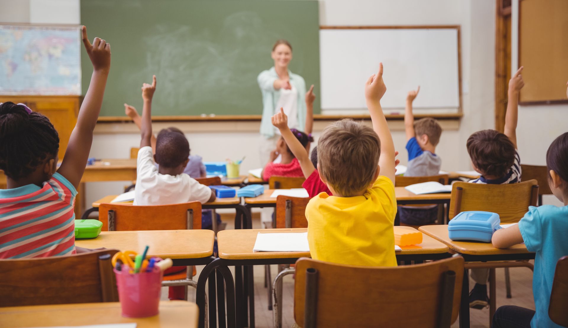 a group of children are raising their hands in a classroom to answer a question .
