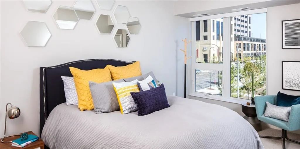 Bedroom with bed, pillows, wall mirrors, chair, and a city view through the window.