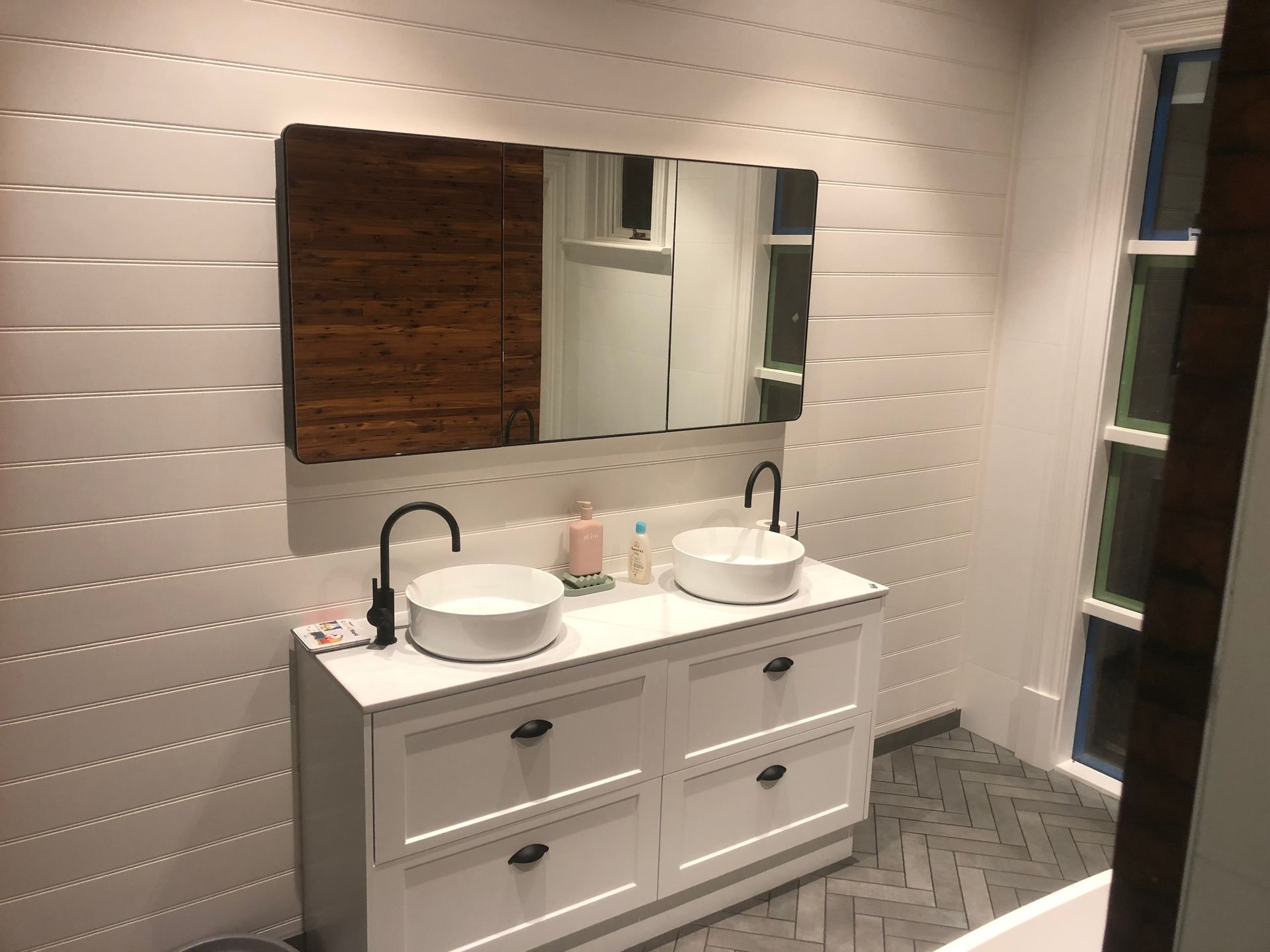 White bathroom with a double sink vanity, large mirror, and black fixtures.
