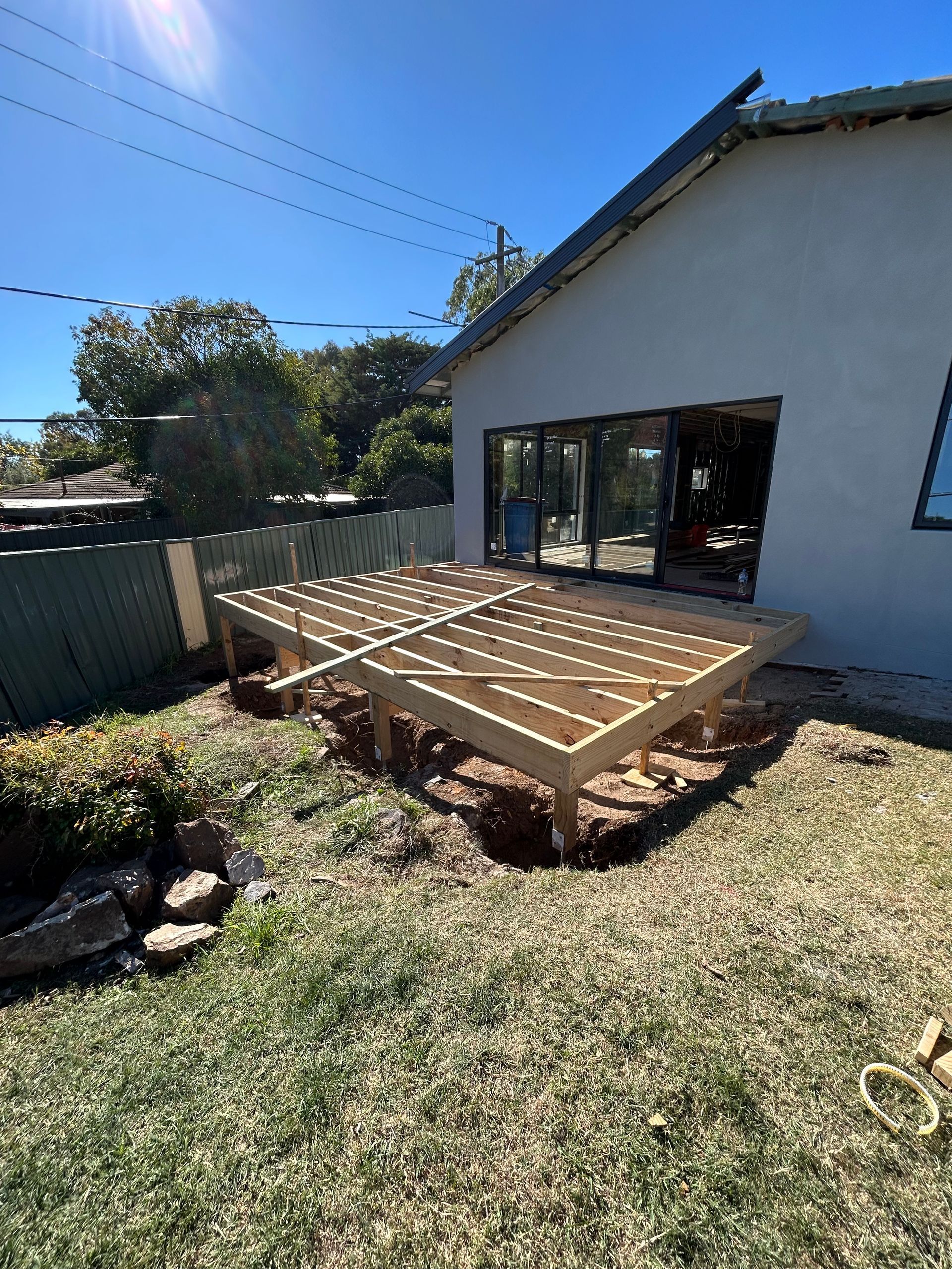 Wooden deck frame under construction next to a house with large sliding doors.