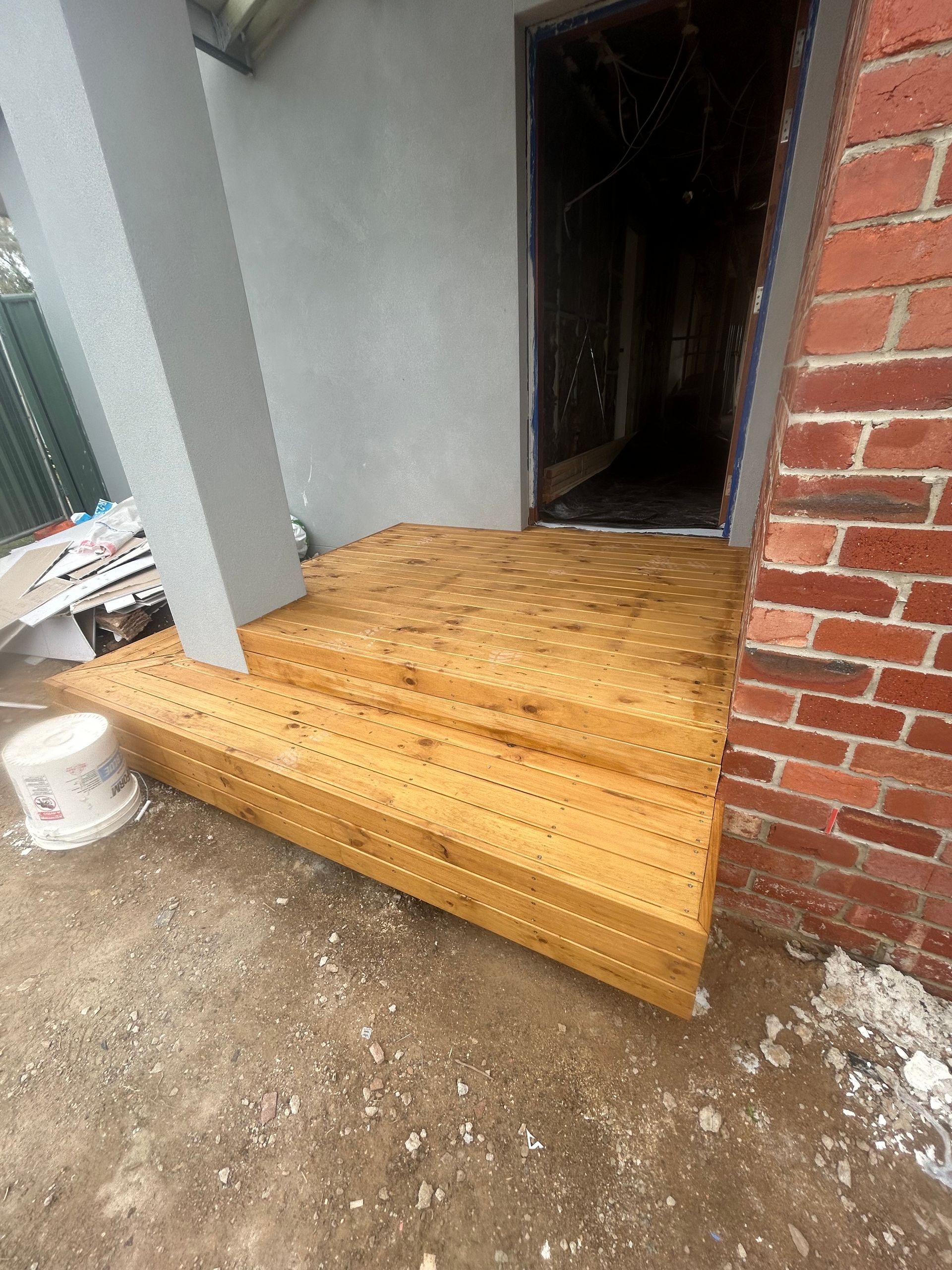 Wooden steps leading to a doorway, with a pillar on the left and brick wall on the right.