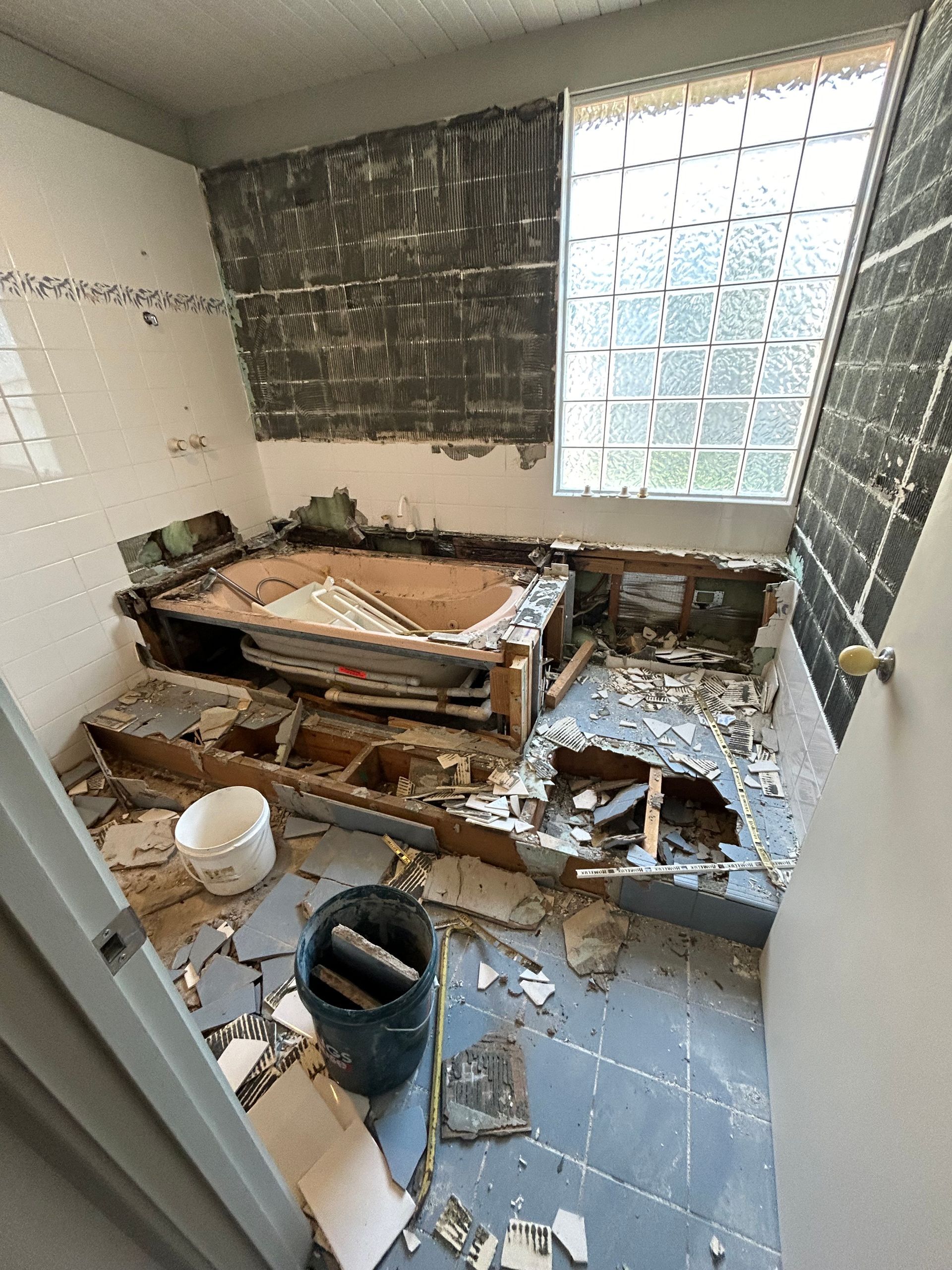 Bathroom under renovation; debris covers the floor. Demolished tub and tile surround. Window visible.