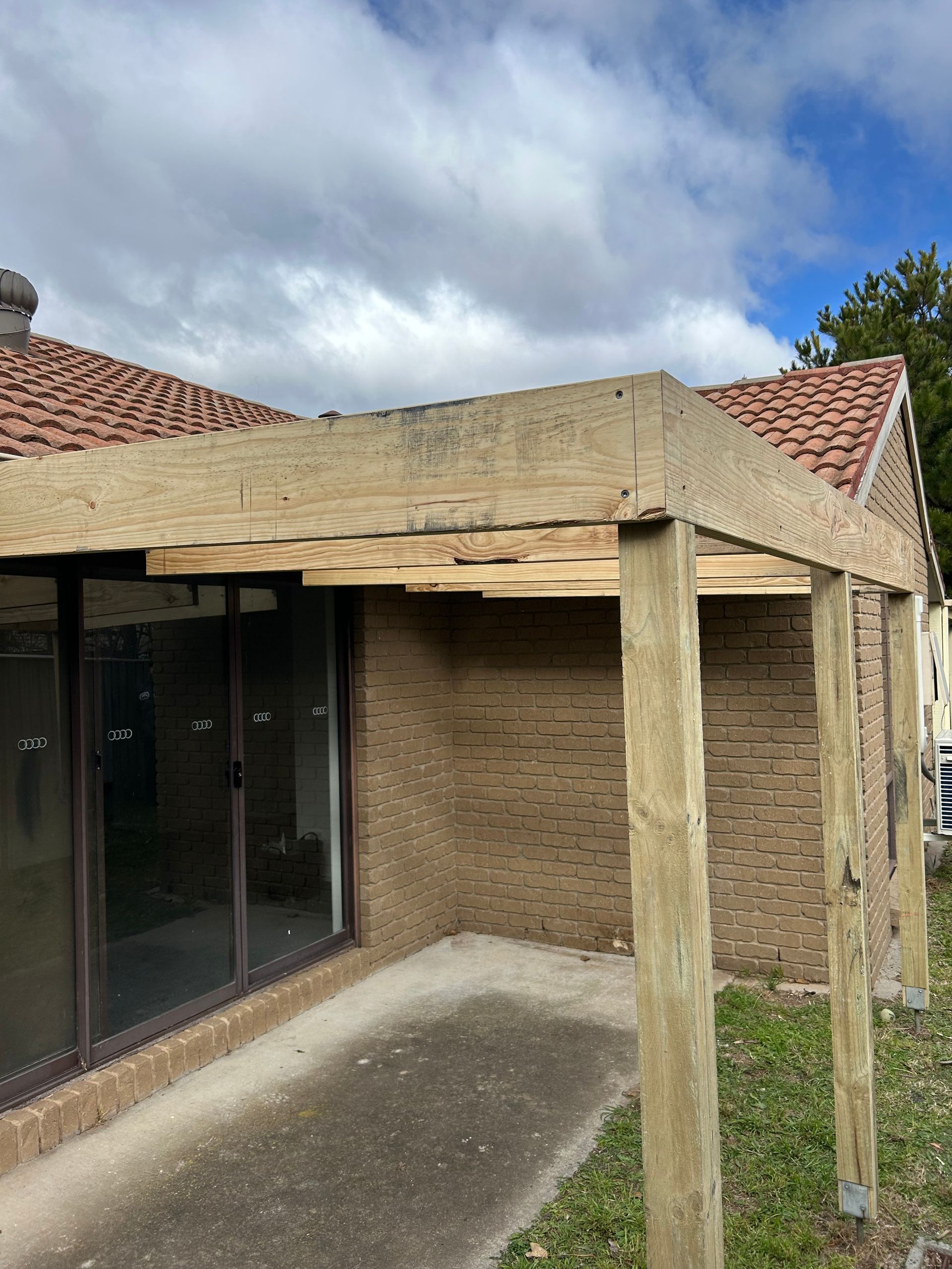 A partially constructed wooden structure attached to a brick building. The roof is visible.