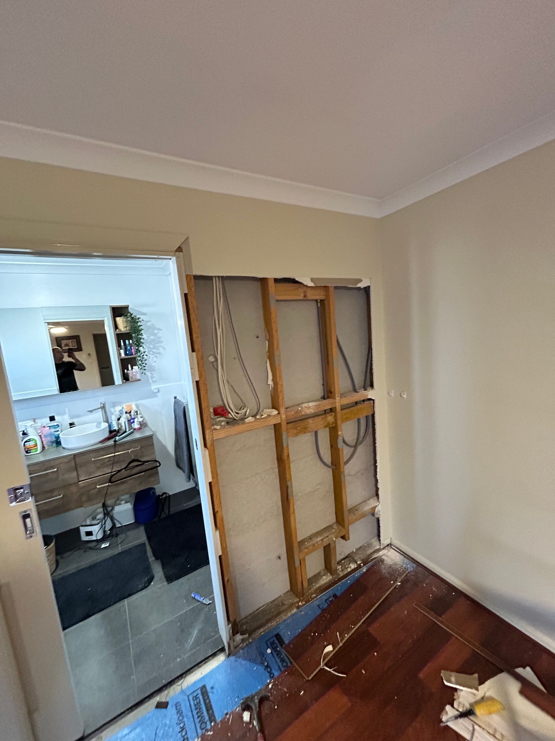 Room with a wall opening into a bathroom. Exposed wall studs and wiring. Damaged flooring.