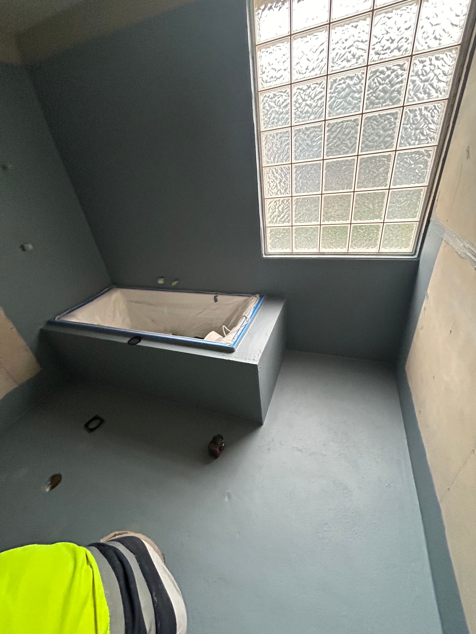 Bathroom renovation in progress, featuring a built-in tub, blue walls, and a glass block window.