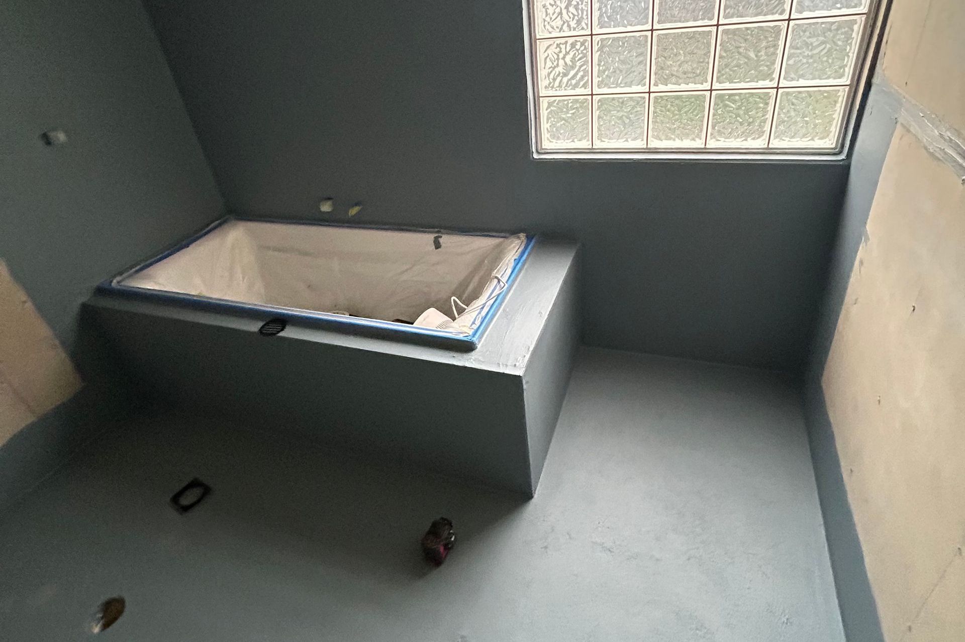 Bathroom with built-in tub, blue walls, a small glass block window, and concrete flooring.