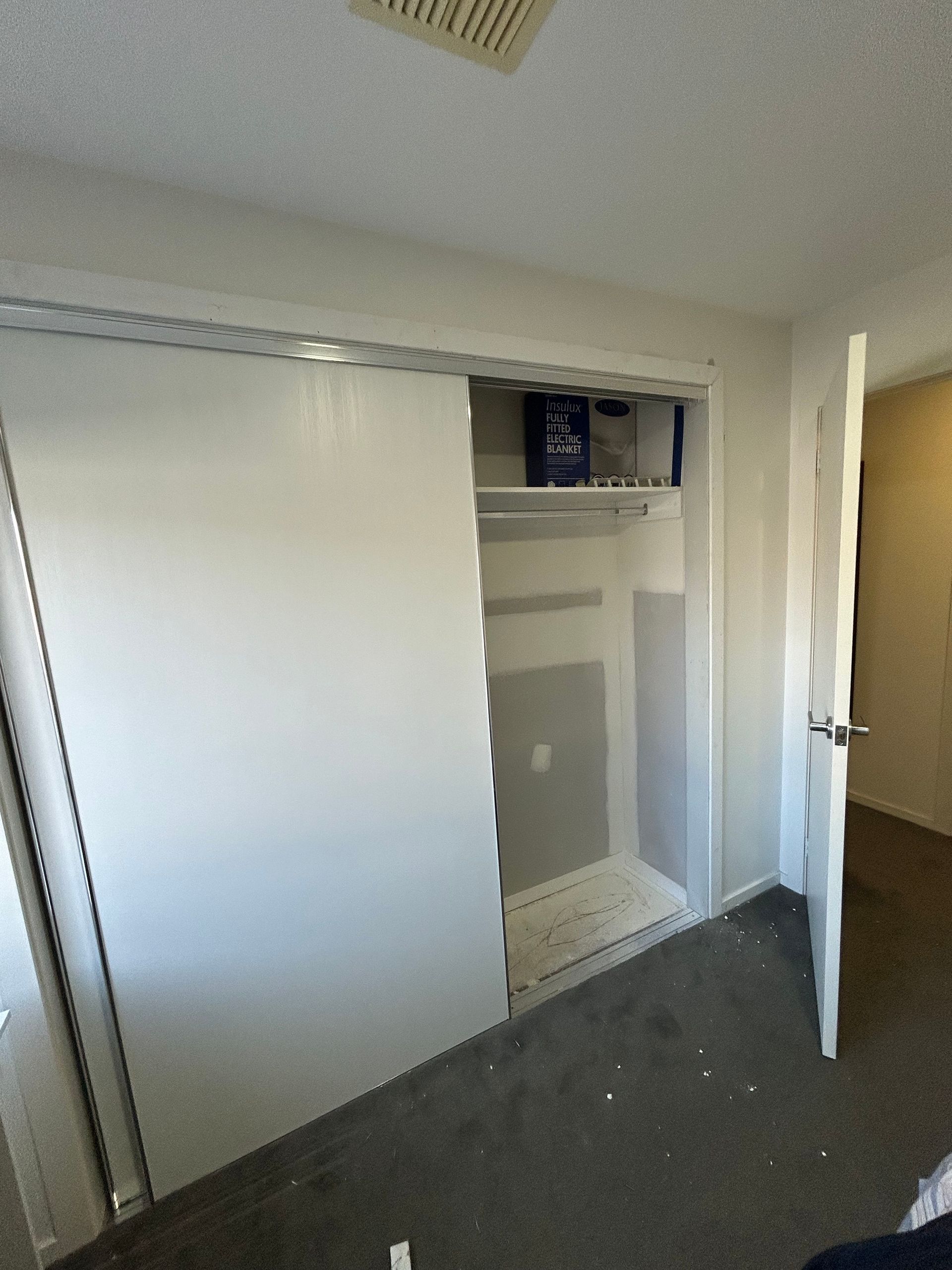 Closet with a sliding door slightly open. White walls, a shelf with items, and a partially open door.