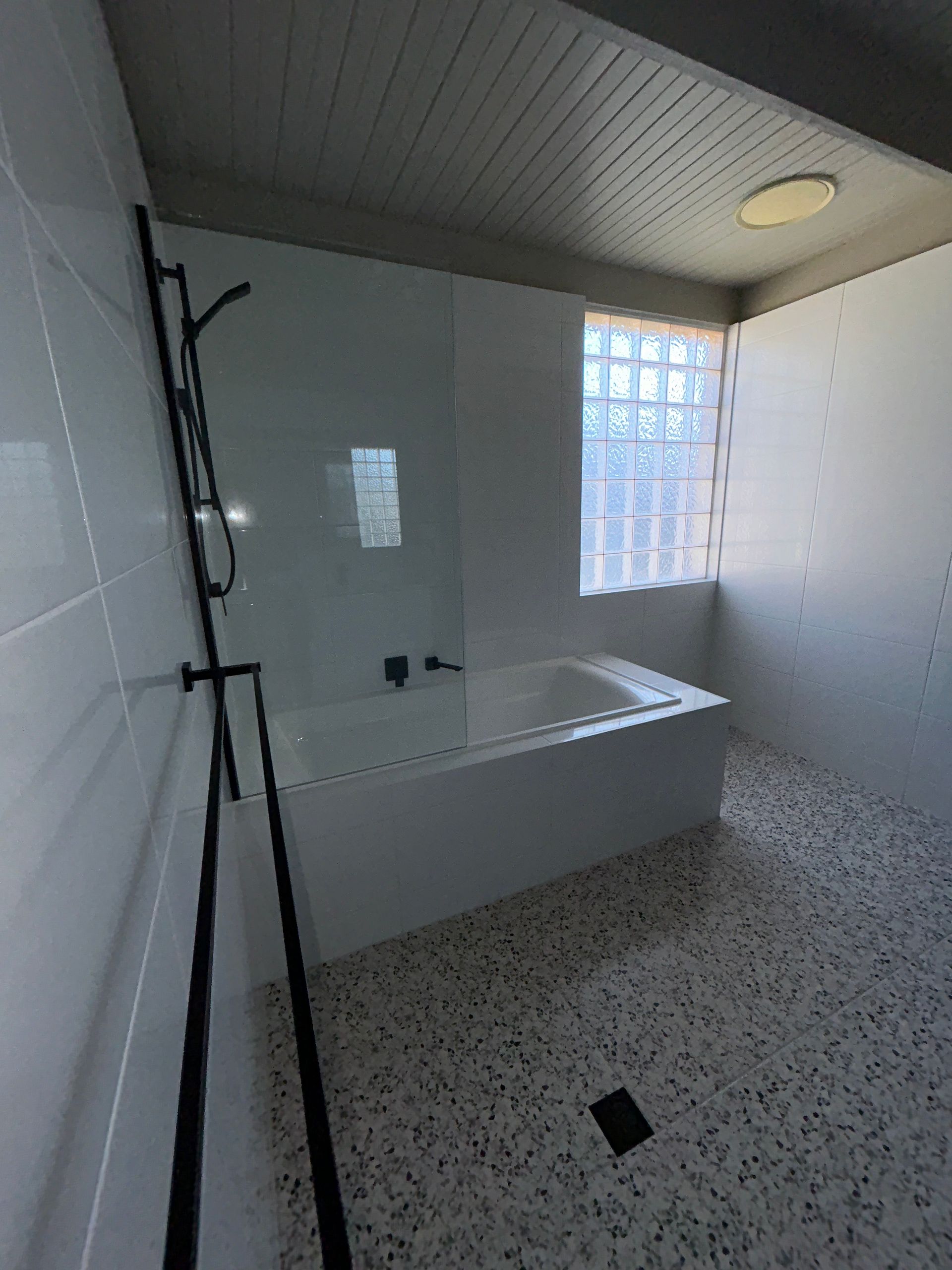 White bathroom with a bathtub, black shower fixtures, and a glass block window.