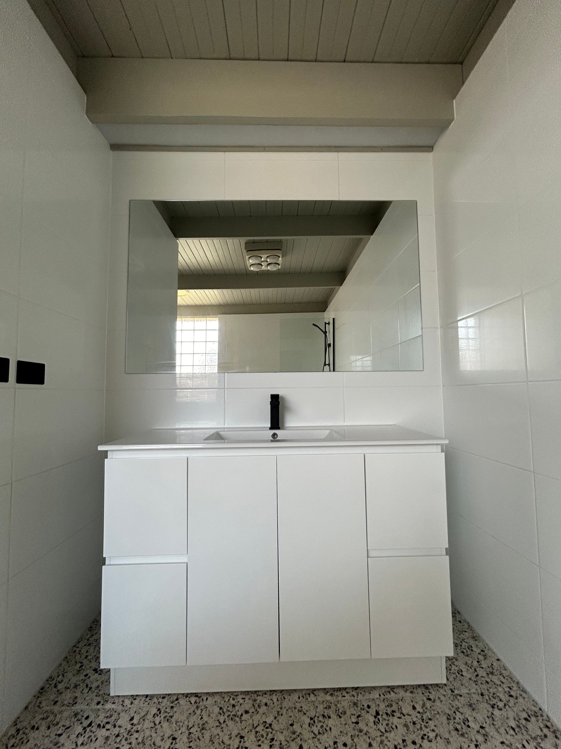 Bathroom with white vanity, large mirror, and black faucet. Tile walls and terrazzo floor.