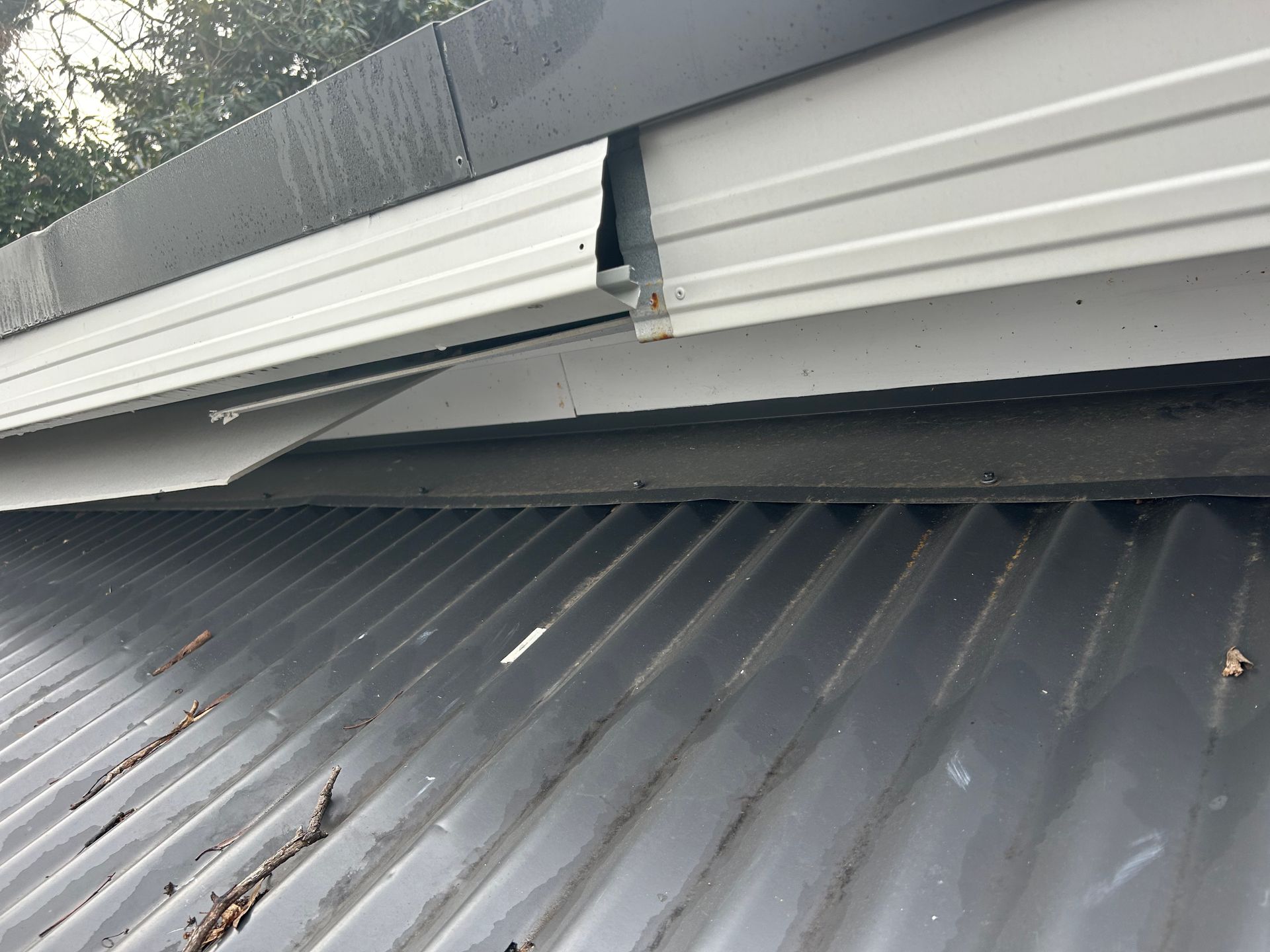 Damaged white metal fascia and guttering on a gray corrugated metal roof.