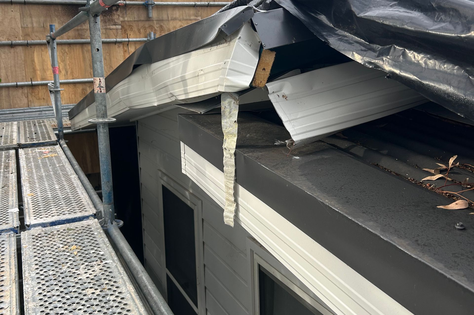 Damaged roof and siding, covered in black tarp, with scaffolding beside the structure.
