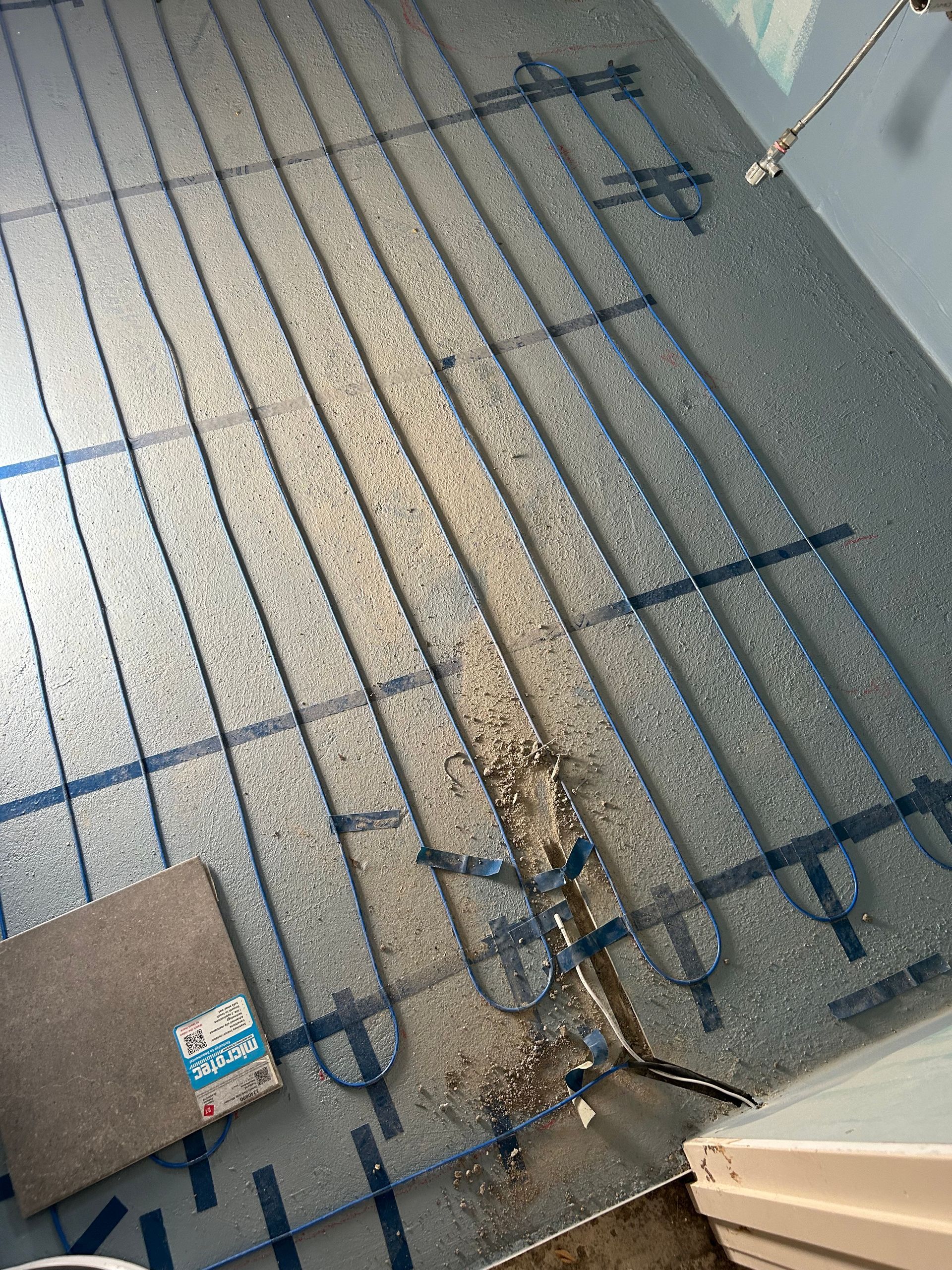 Blue radiant floor heating cables laid on a gray surface, with a tile sample.